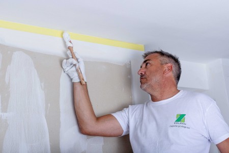 Peintre entrain de peindre les bords du plafond en blanc après avoir posé ruban de masquage - Zolpan